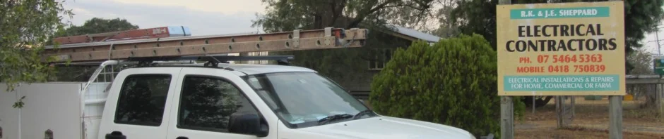 A white Sheppard work ute with ladder racks parked beside the R.K. and J.E. Sheppard Electrical Contractors sign in Walloon